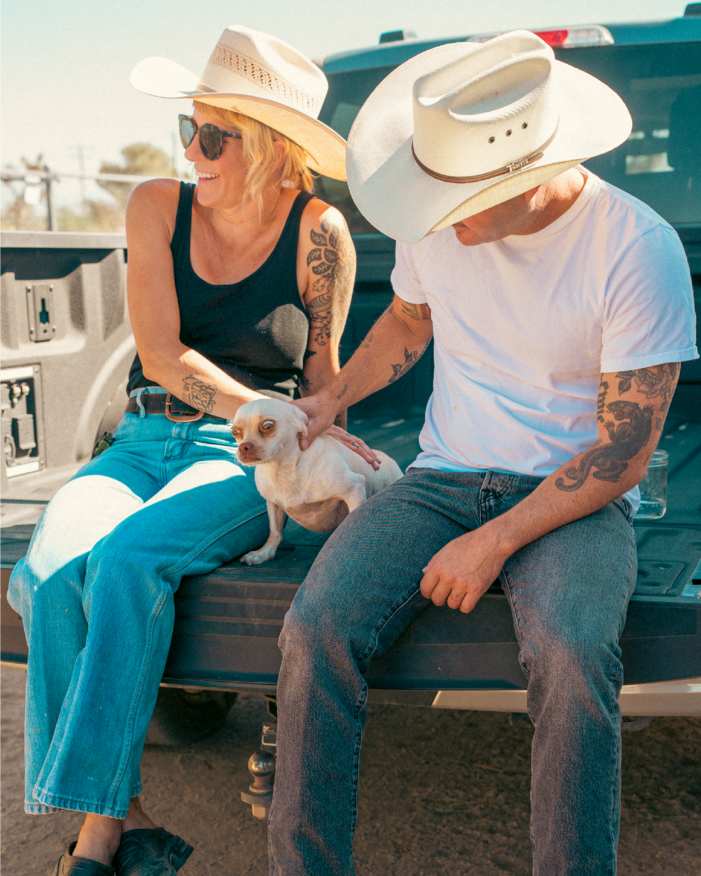Couple in cowboy hats relaxing in the back of a truck with their small dog, embodying the Western lifestyle and comfort that Westech Outrider shoes are made for, Made in USA