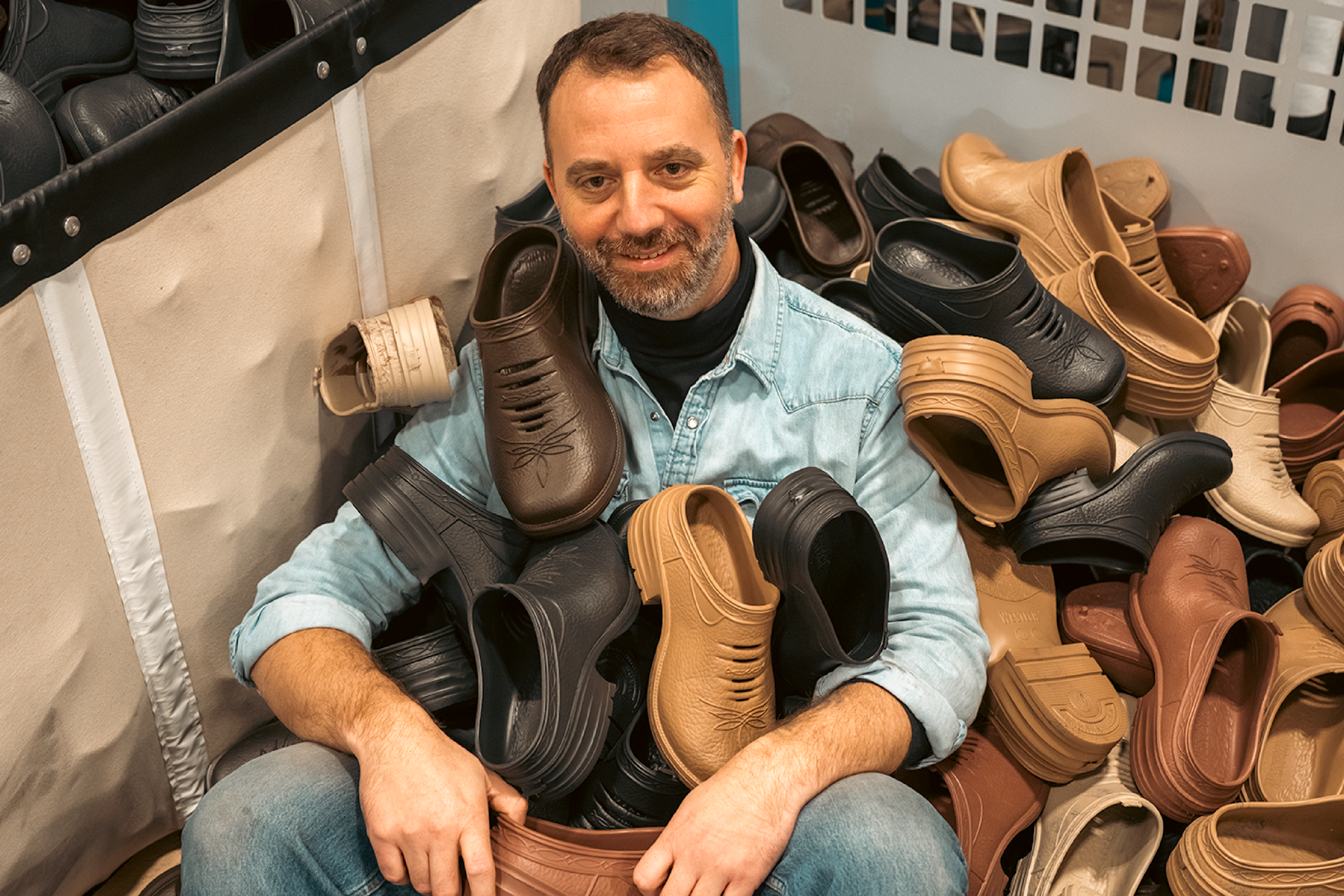 Man sitting in a bin full of Westech Outrider shoes in multiple colors, smiling and surrounded by inventory, representing the variety and comfort of our Made in USA Western footwear